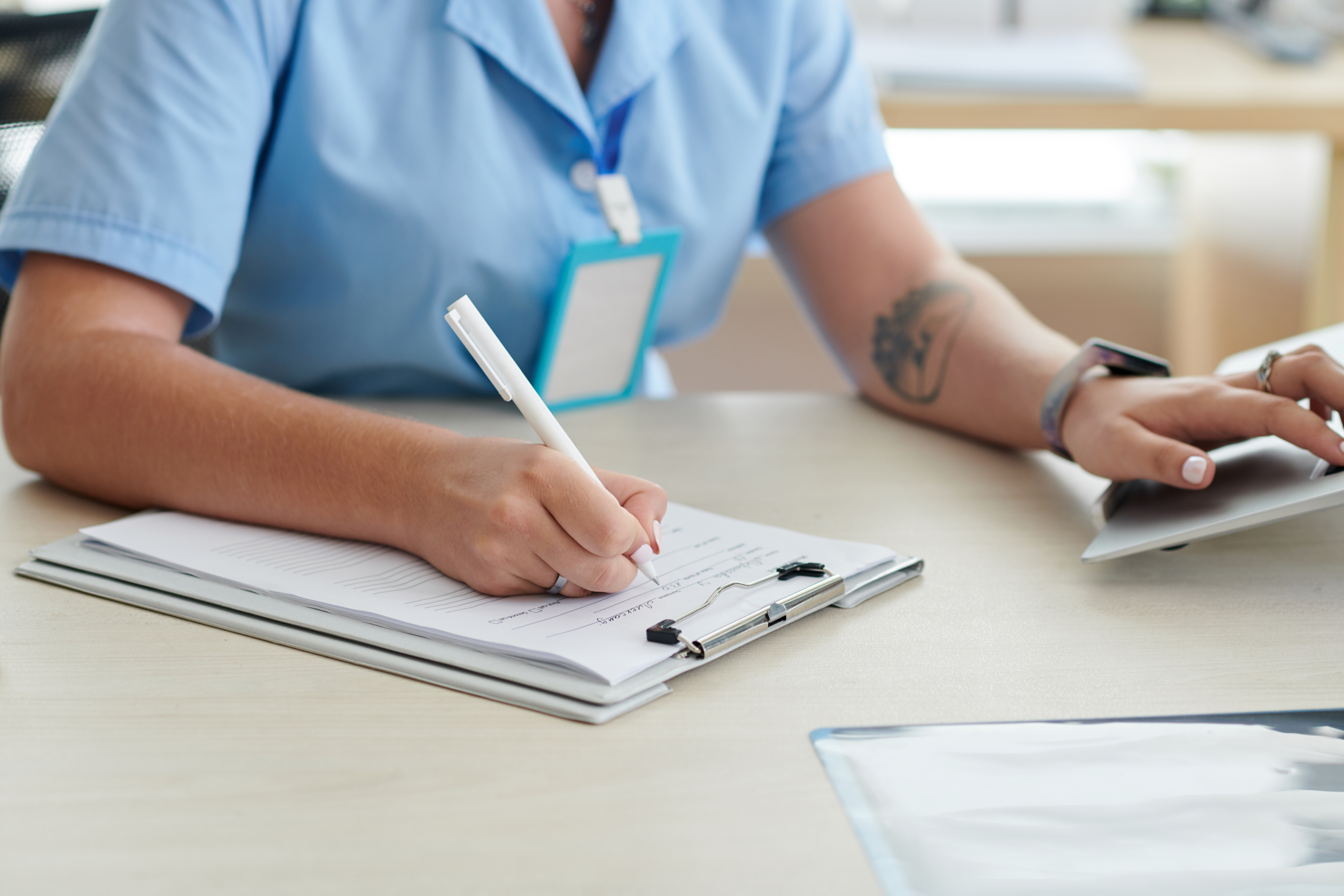 Close-up of female doctor sitting at table at office and filling patient card