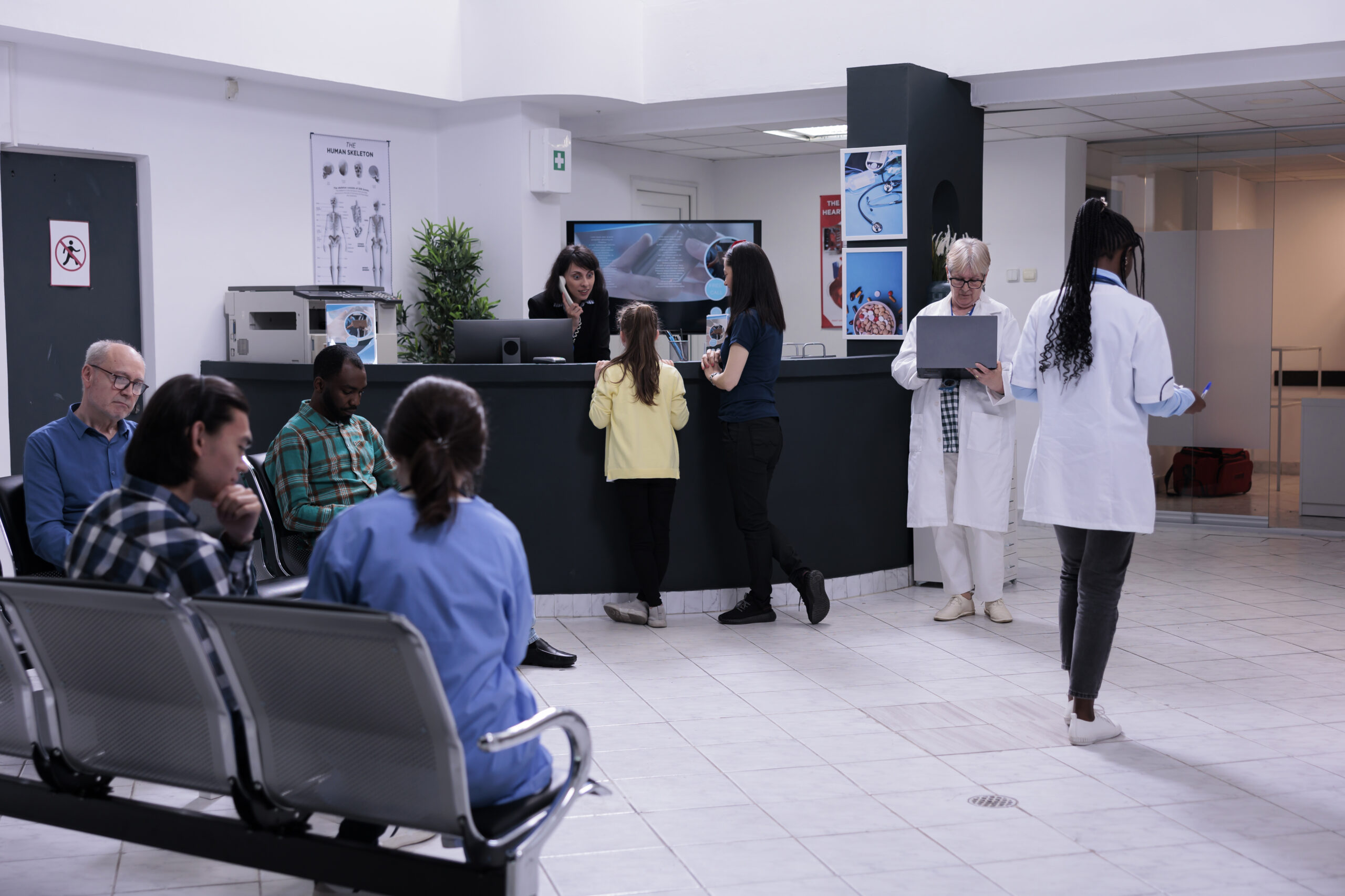 Front desk receptionist talking with young girl patient registering for doctor appointment with her mother Front desk receptionist talking with young girl patient registering for doctor appointment with her mother in private hospital. Nurse talking with diverse patients waiting in modern clinic.